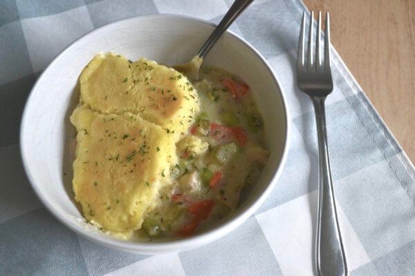chicken pot pie in a white bowl on a checkered tablecloth with a fork beside it.