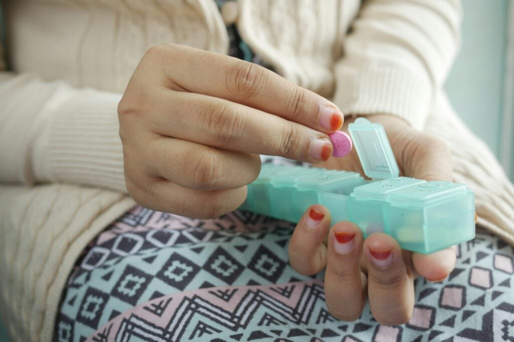 A close-up of someone's hands as they are putting pills into a pill organizer