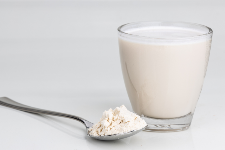 A spoon filled with a white powder is sitting next to a glass that is filled with a mixed nutritional drink