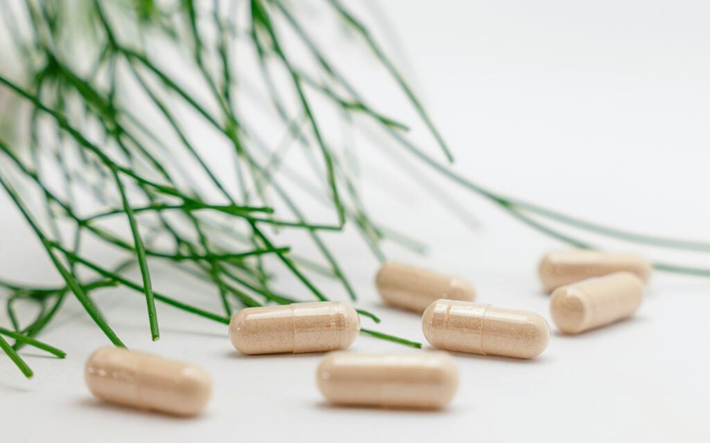 Seven supplement capsules sitting on a white countertop with a green plant in the background